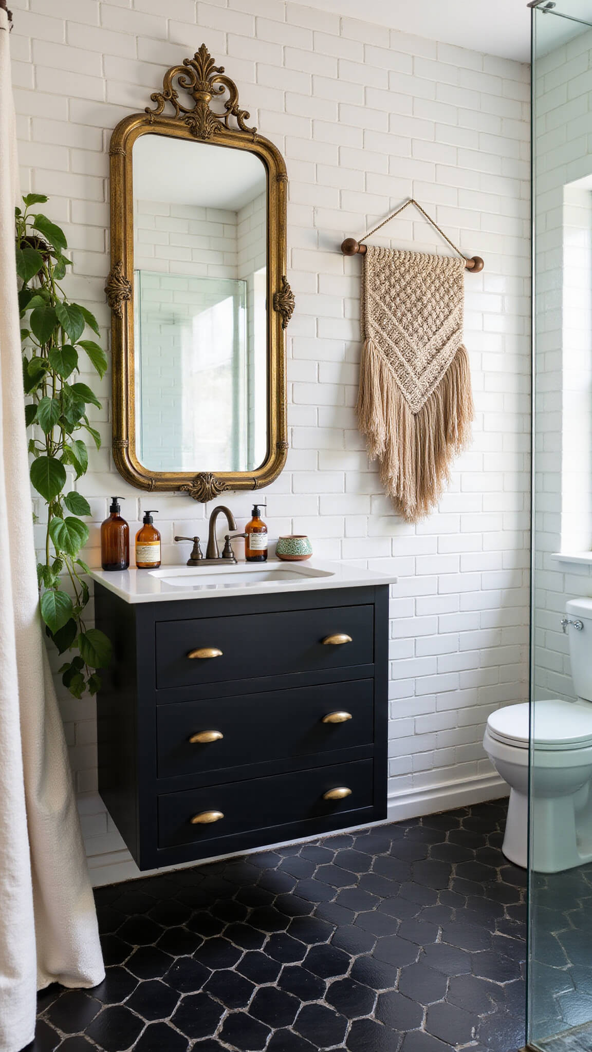 Modern boho minimalist bathroom with black hex tile floor, white subway walls, matte black floating vanity, brass mirror, cascading pothos plant, and geometric woven wall hanging.