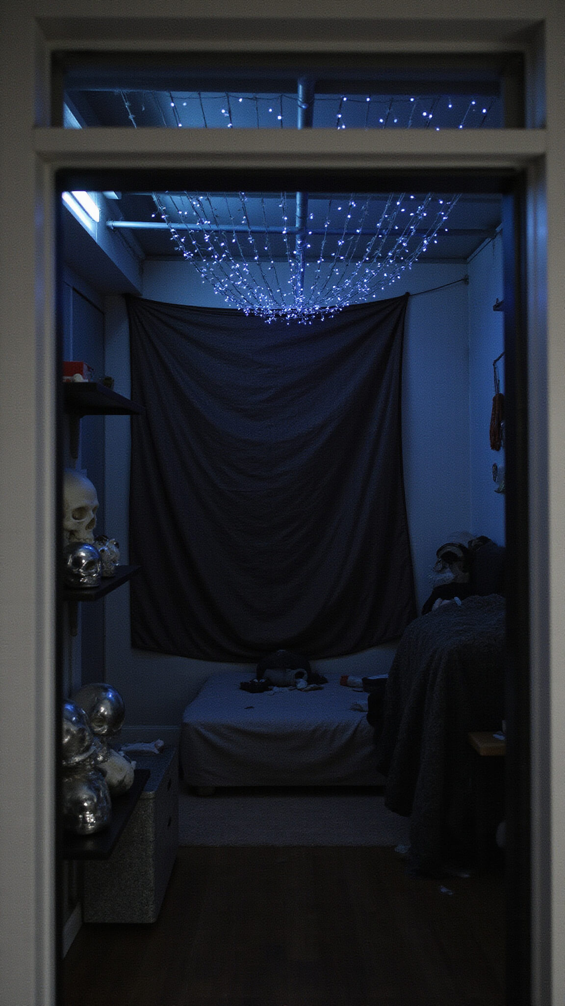 Late night loft interior with constellation-like string lights, textile headboard, skull-themed decor on floating shelves, and moody low lighting in dark blue, silver, and red tones.