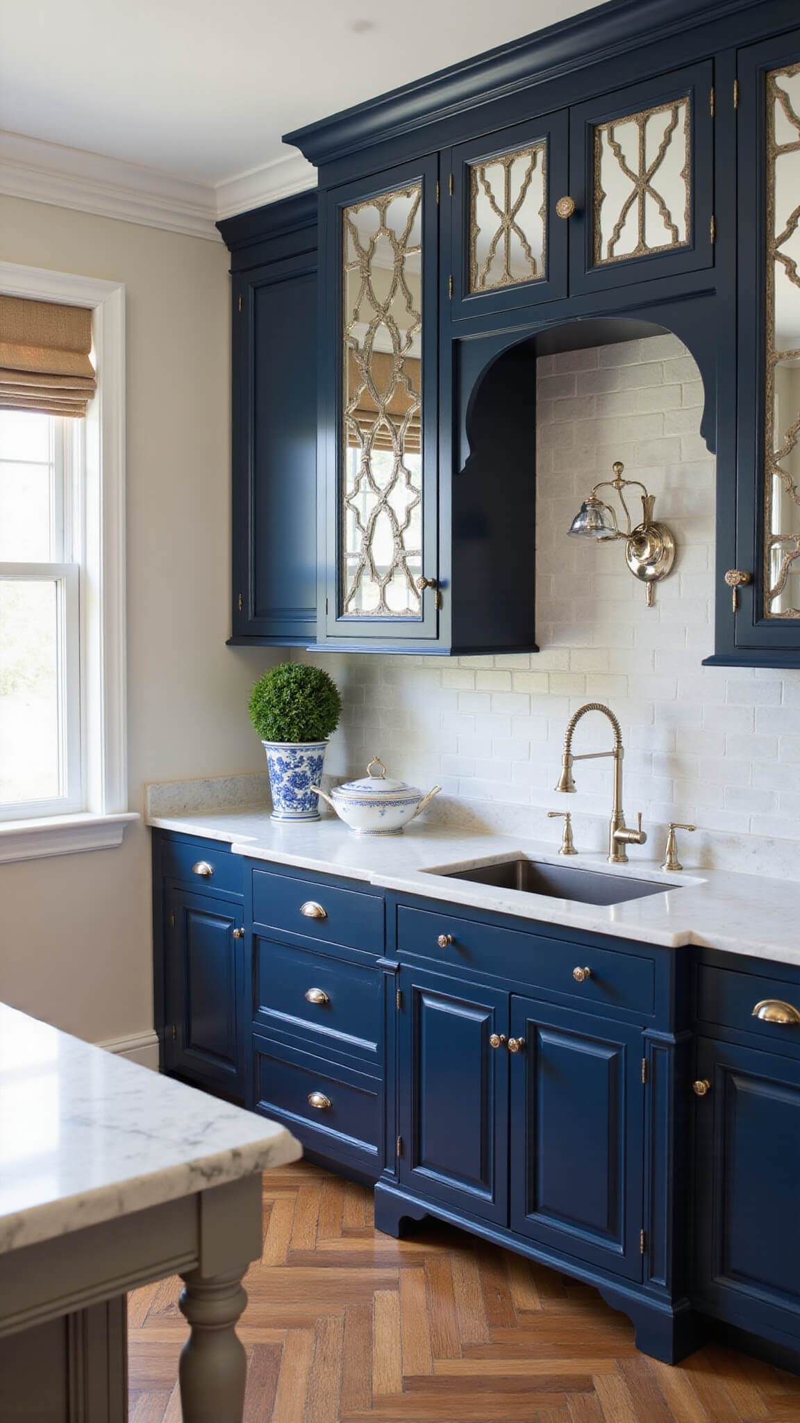 Traditional navy kitchen with marble countertops, antique mirror cabinets, chinoiserie planters, silver tea set, and herringbone wood floors.