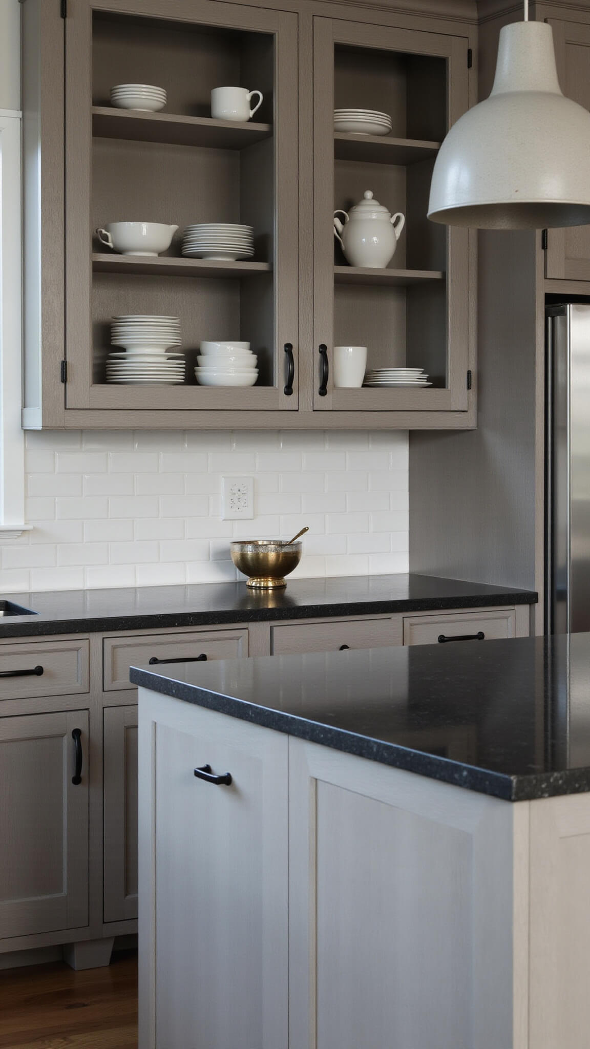 Macro of modern farmhouse kitchen with gray wood cabinets, black countertop, matte black handles, and glass doors displaying white dinnerware in dramatic afternoon light.