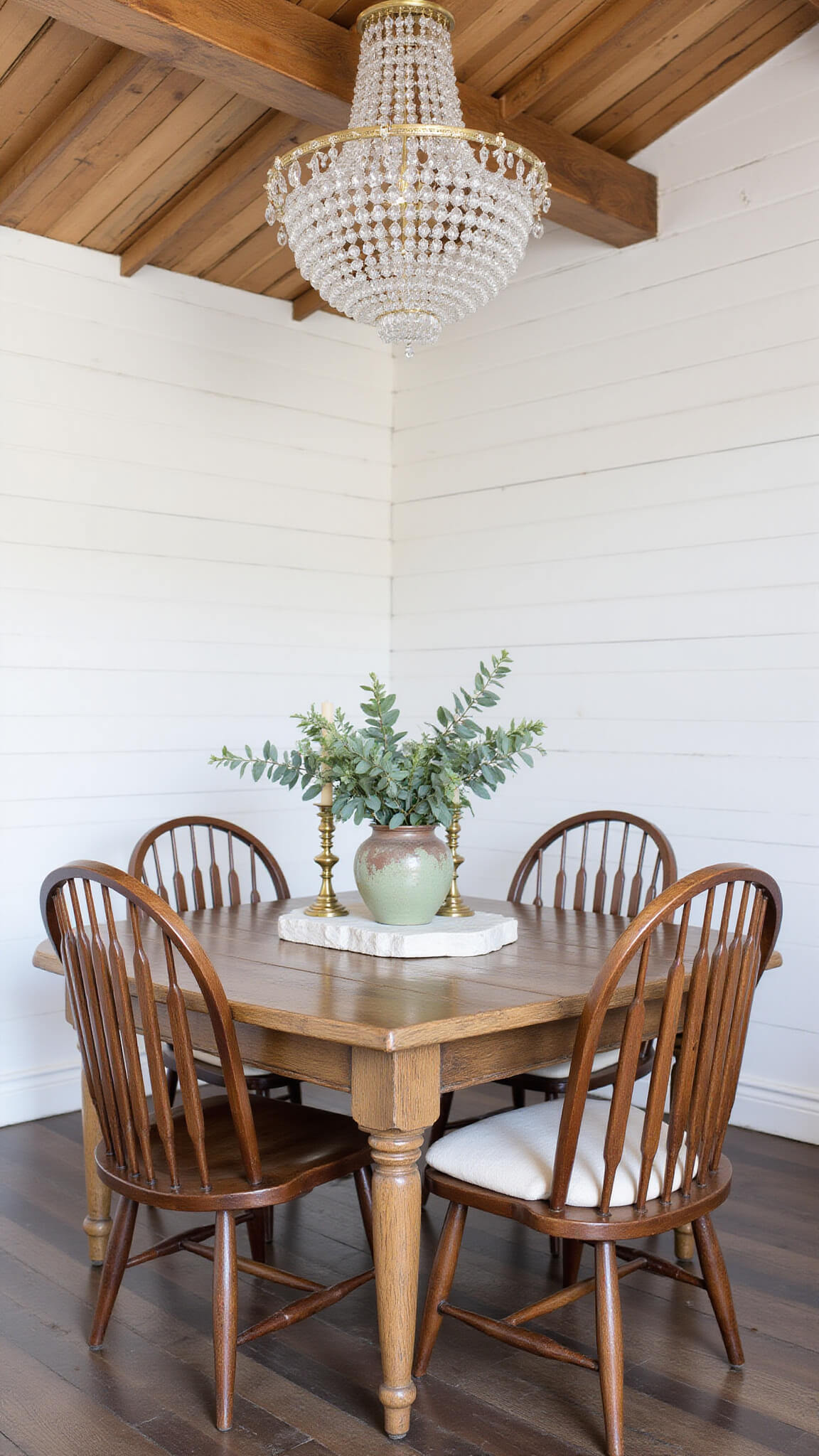 Farmhouse dining room with reclaimed wood table, mixed chairs, vintage chandelier, white plank walls, and rustic decor.