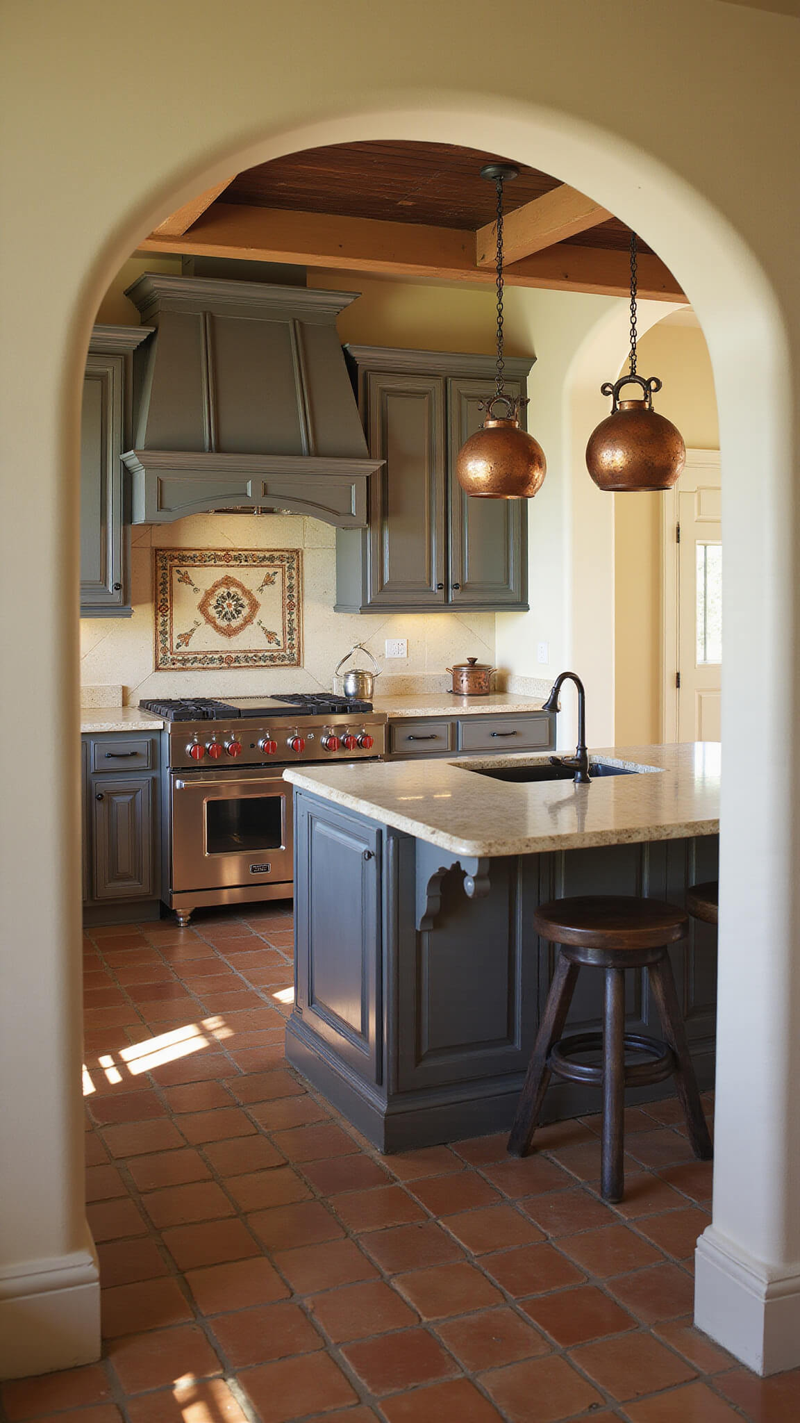 Mediterranean kitchen with distressed charcoal gray cabinets, terracotta floor tiles, limestone counters, hand-painted backsplash, and copper pots under warm late afternoon light.