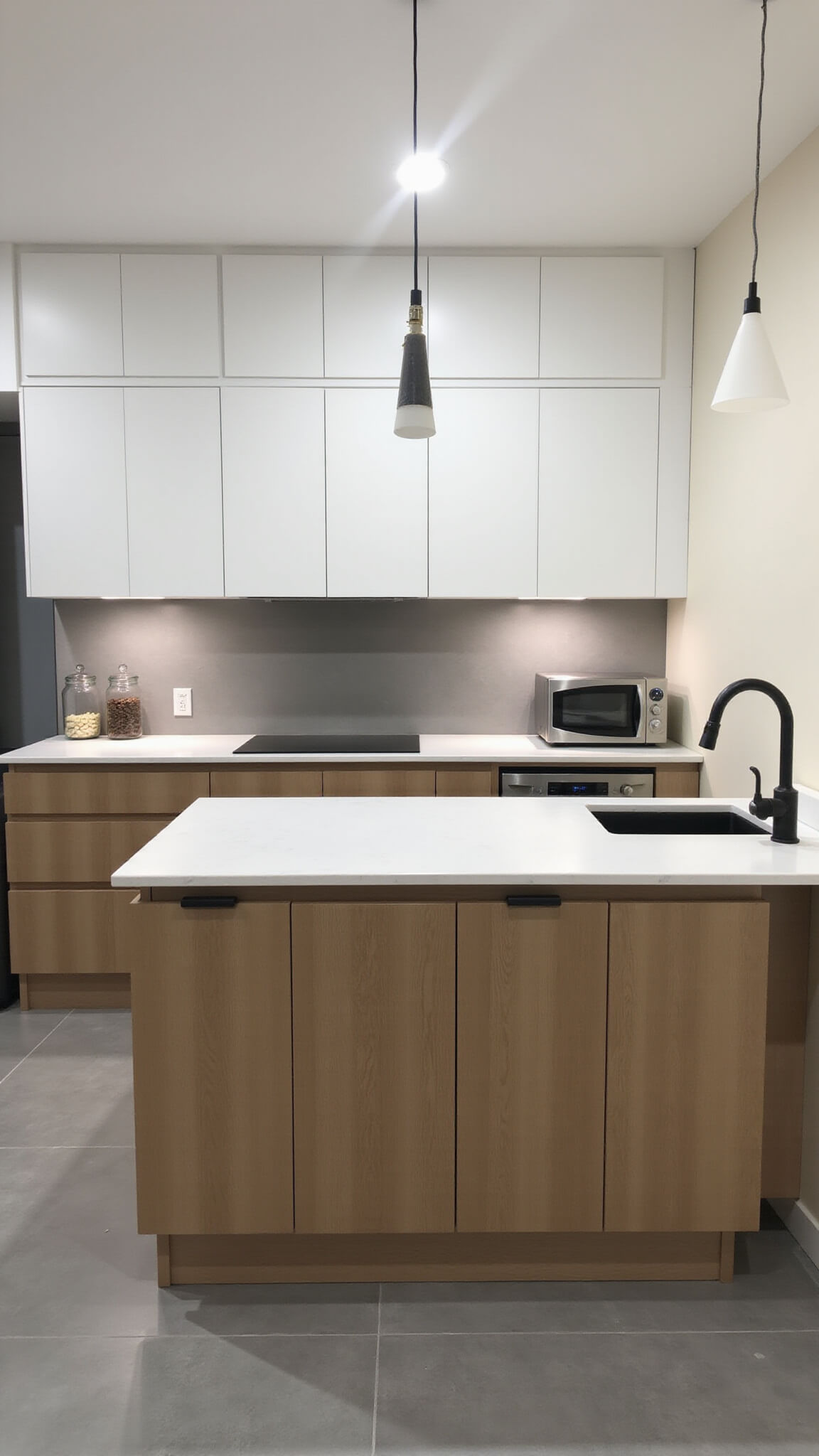 Contemporary 12x14ft kitchen with light brown lower cabinets, floating white uppers, waterfall quartz island, matte black fixtures, and grey floor tiles under dusk LED lighting.