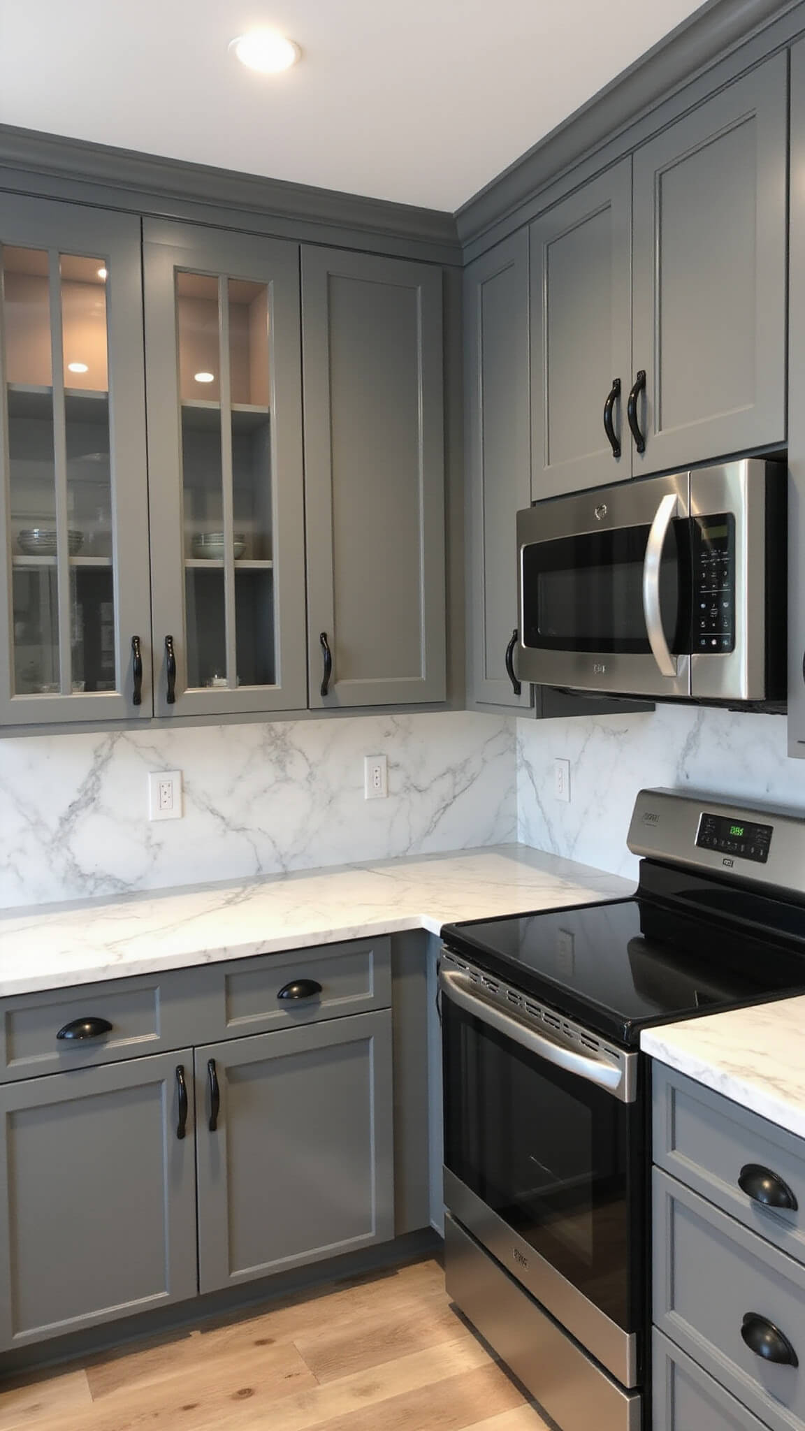 Professional kitchen with slate grey cabinets, white marble countertops, stainless appliances, and glass-front lit uppers under studio lighting.