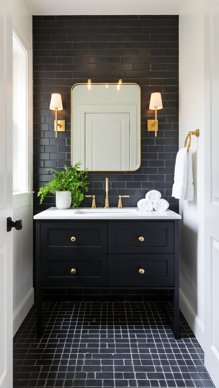 Small modern bathroom with dark charcoal tiles, white walls, black wall-mounted vanity, backlit mirror, brushed gold fixtures, emerald green plants, and white towels.