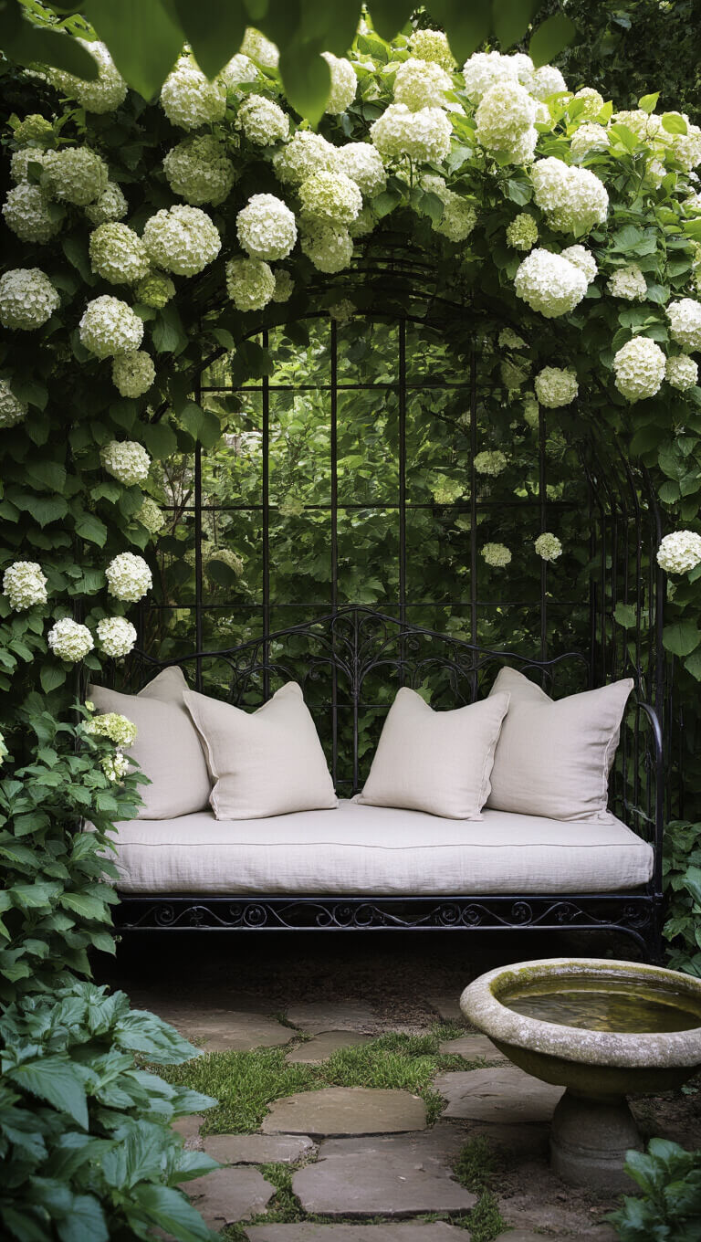 Cozy secret garden reading nook at dusk with vintage iron daybed under hydrangea-covered arbor, seen through soft foliage with nearby stone bird bath.