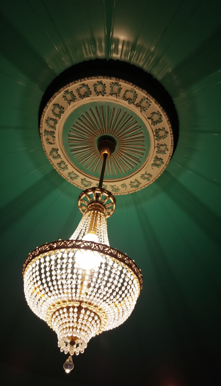 Art Deco ceiling medallion with crystal chandelier on emerald green lacquered ceiling, viewed from below with dramatic lighting and shadows.